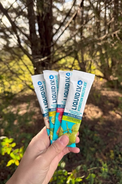 A close-up shot showing four individual electrolyte drink mix sticks being held against an outdoor, sunlit background.
